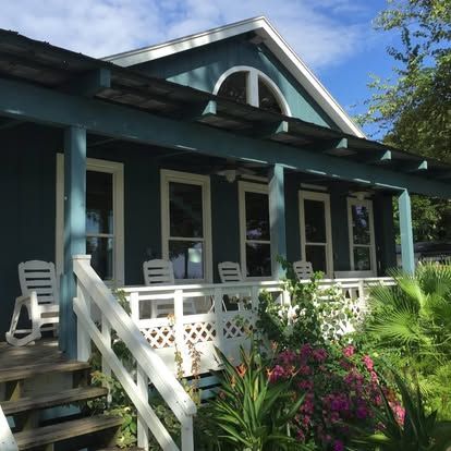 Blue cottage porch with white trim, rocking chairs, and pink flowers in the front garden