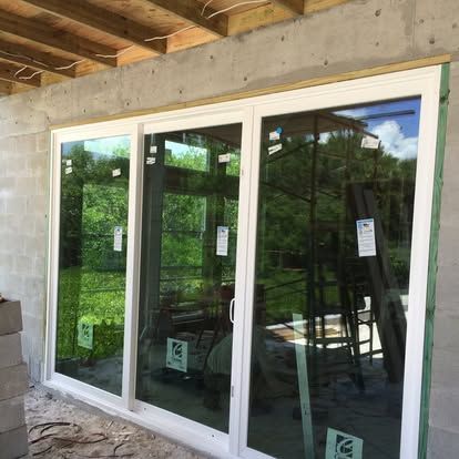 Three-panel sliding glass door installed in a concrete wall, with wood framing visible above.
