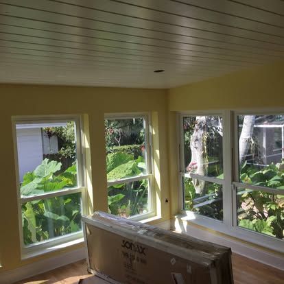 Sunlit empty room with large windows overlooking lush green garden and a wrapped box on the floor