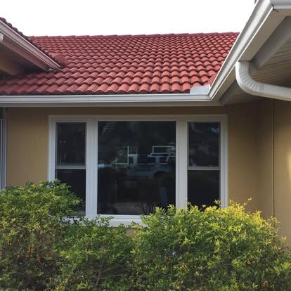 House with red tile roof, white-trimmed window, and shrubs in the foreground