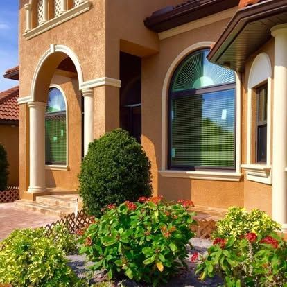 Sunlit stucco house exterior with arched windows and colorful front garden shrubs