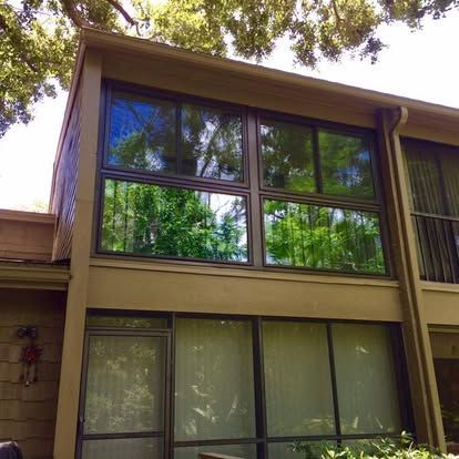 Two-story house facade with large tinted windows and trees reflected in the glass