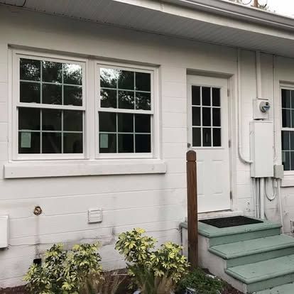 White house exterior with double windows, front door, green steps, and small shrubs.