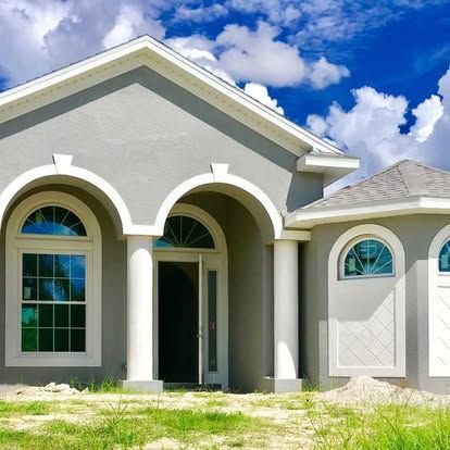 Single-story gray house with arched porch columns, white trim, and blue sky above