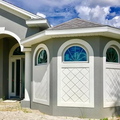 Front entrance of a light gray house with arched windows and a white-trimmed octagonal bay