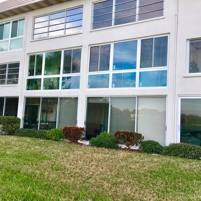 Modern white apartment building with large windows, shrubs, and a grassy lawn