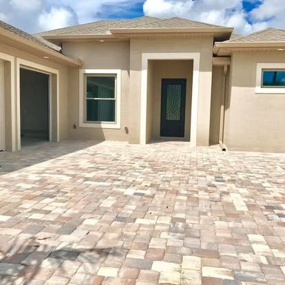 Modern beige house courtyard with tiled driveway, front door, and garage under a blue sky