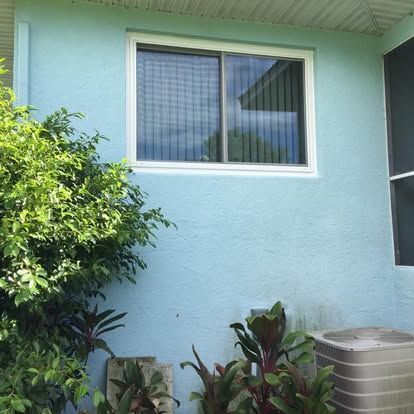 Blue stucco house wall with a window, shrubs, and an air conditioner unit