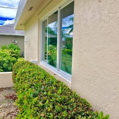 Beige house exterior with large sliding windows and a trimmed green hedge along the wall