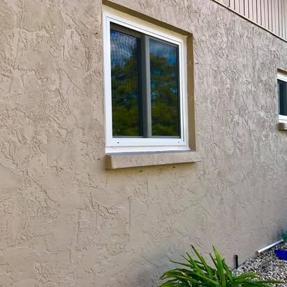 White-framed window on a beige stucco exterior wall with plants below