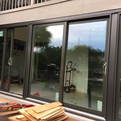 Stacked wooden boards in front of large sliding glass doors reflecting an outdoor patio.