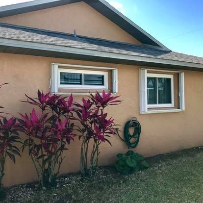 House exterior with peach stucco wall, two white-framed windows, and red-leaf plants by the lawn