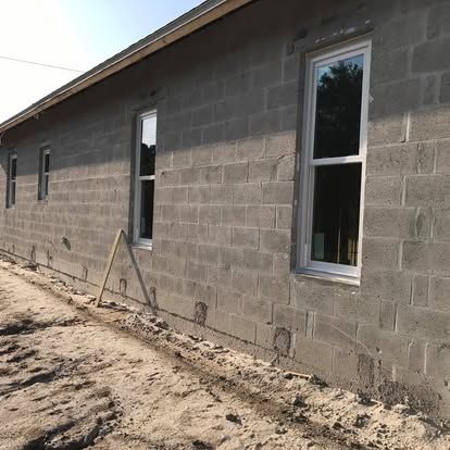 Unfinished gray cinder block house wall with two windows and a dirt yard in front