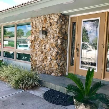 Front entrance of a home with stone wall, tan door, windows, and potted plants
