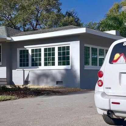 White house exterior with large windows and a parked white SUV in the driveway.