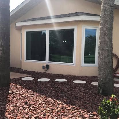 House exterior with three windows, rock landscaping, and a palm tree in front