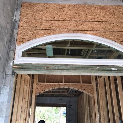 Partially built house interior with framed walls, plywood sheathing, and a white arched window opening