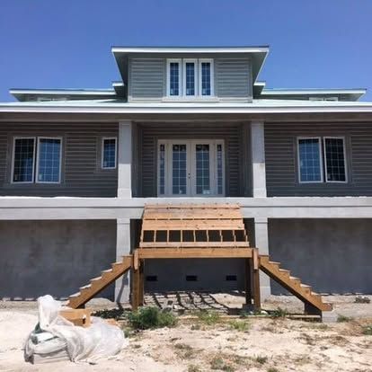 Gray two-story house with a wooden front ramp under construction and debris in the yard