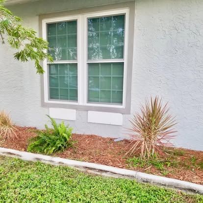 Residential window with white trim above a landscaped bed and green lawn