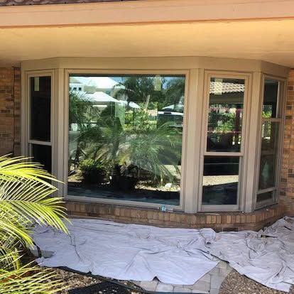 Outdoor bay window with reflective glass, beige trim, and white drop cloths on the ground
