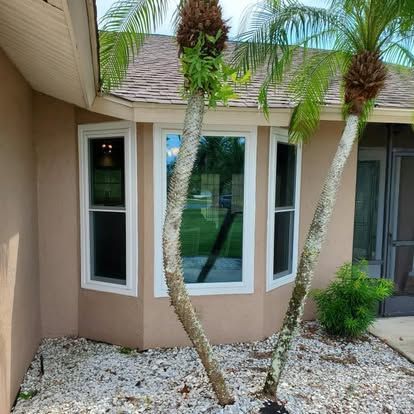 Two palm trees in a gravel bed beside a tan house with bay windows.