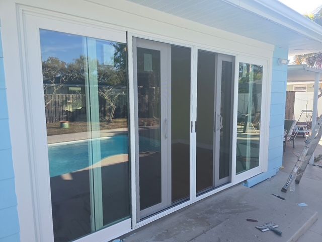 Large white sliding glass doors reflecting a backyard pool beside a house exterior