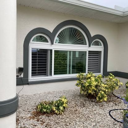 House exterior with arched window, white shutters, and gravel landscaping beside a column.