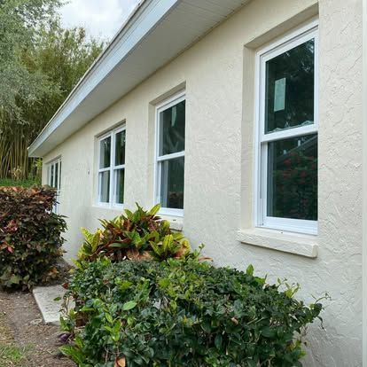 Exterior wall of a house with white-framed windows and green shrubs along the side