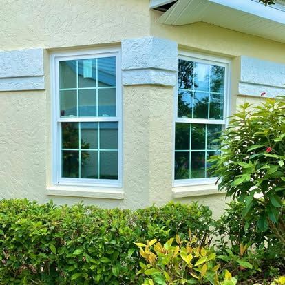 Two white-framed windows on a cream stucco house above a green hedge