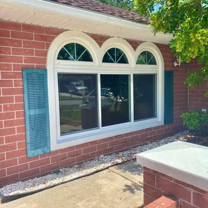 Brick house exterior with arched window, blue shutters, and concrete walkway