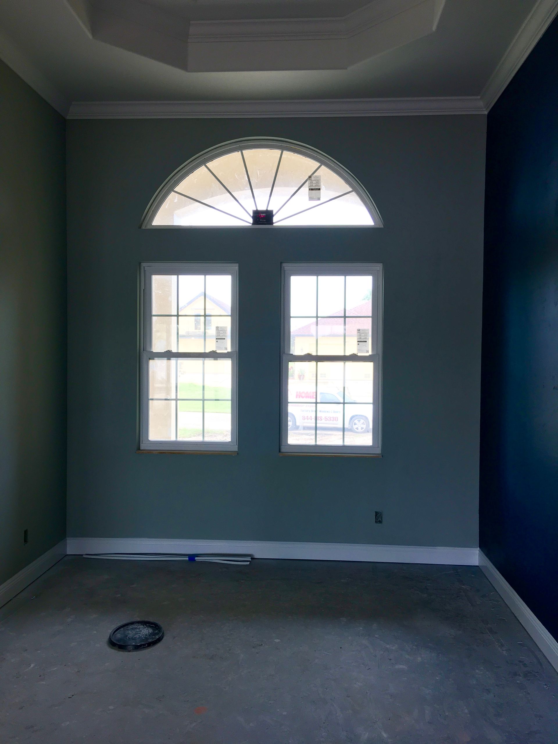 Empty room with gray walls, two windows, and an arched transom letting in daylight.