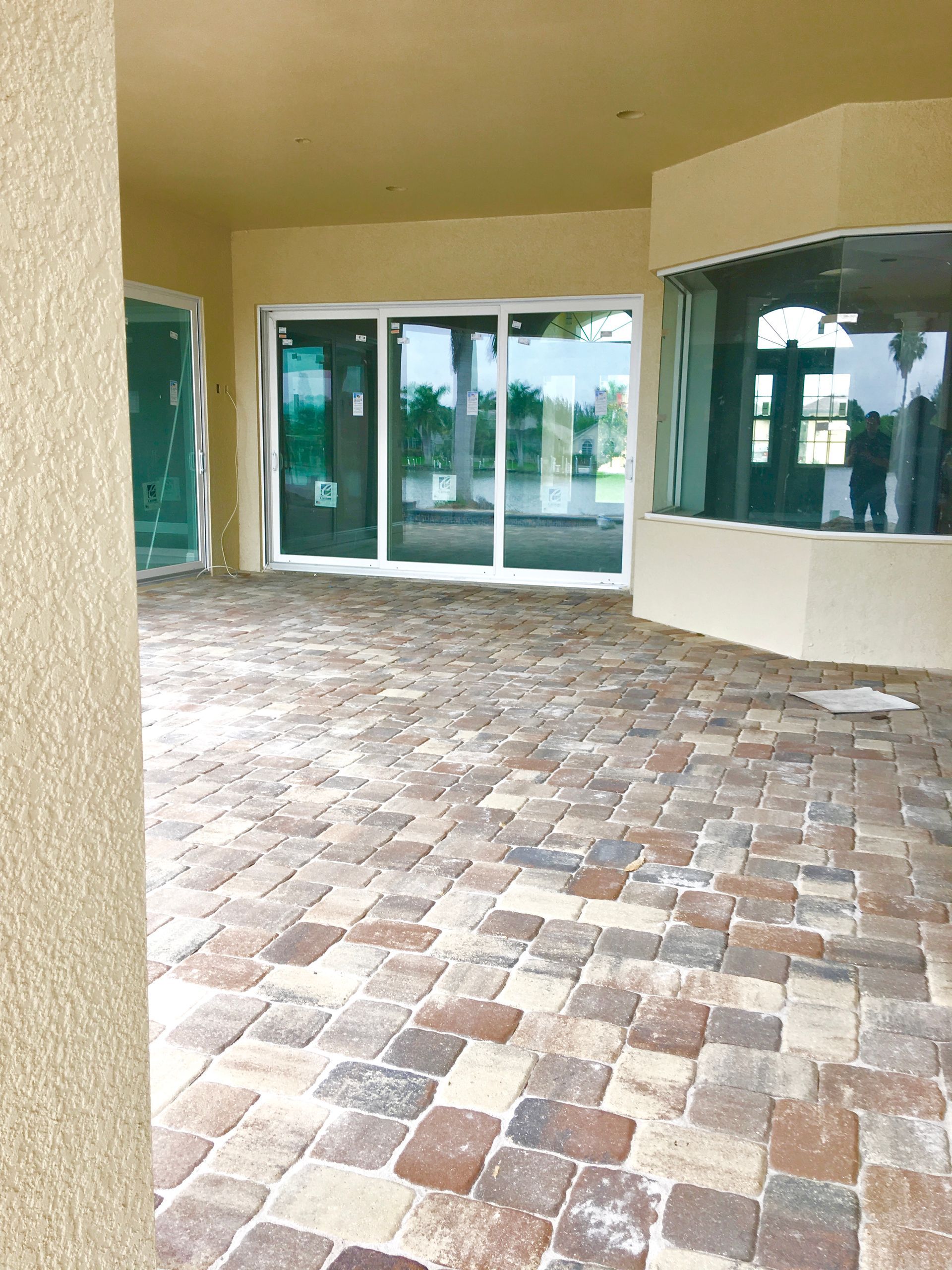 Empty covered patio with brick paver floor, beige columns, and large glass sliding doors.