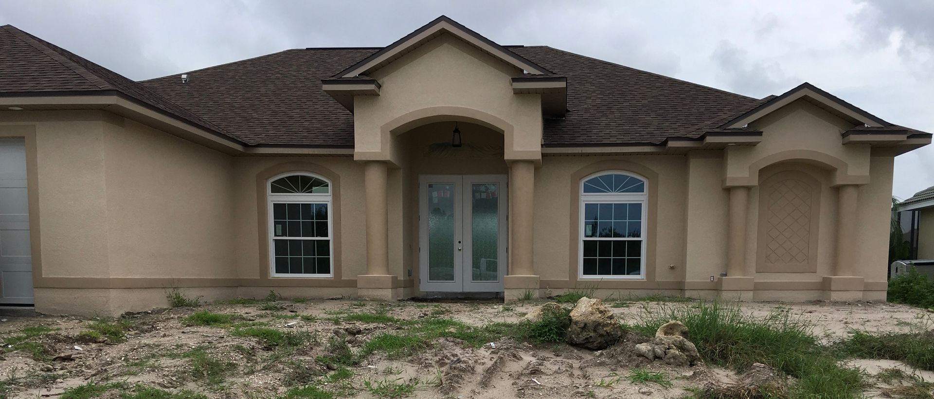 Single-story beige house with a central front entry, arched windows, and a rocky front yard