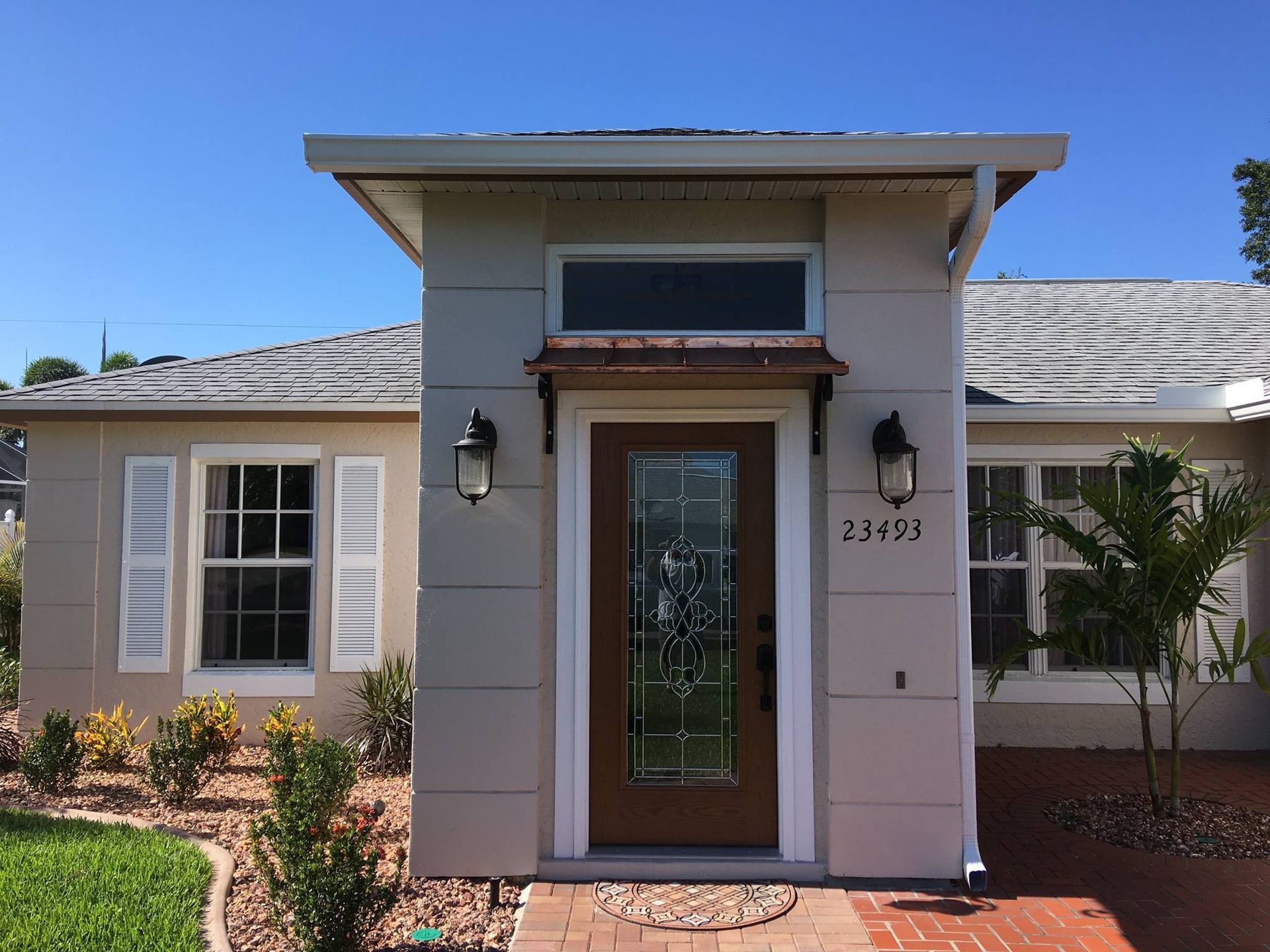 Front entrance of a single-story beige house with white shutters, a glass door, and a small porch.
