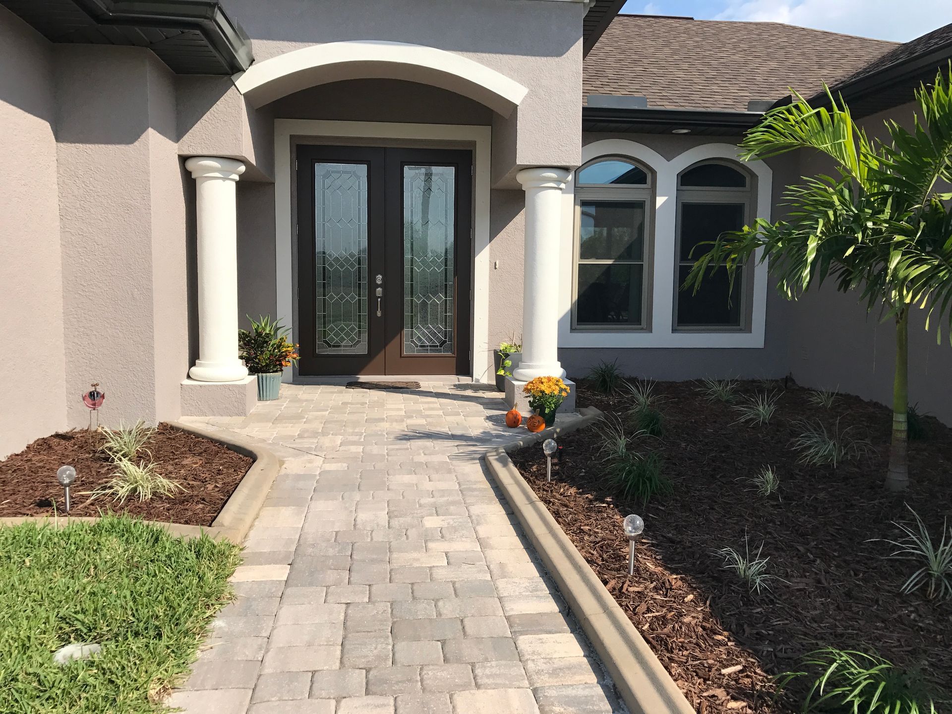 Front entrance of a house with stone walkway, arched doorway, and landscaped garden beds