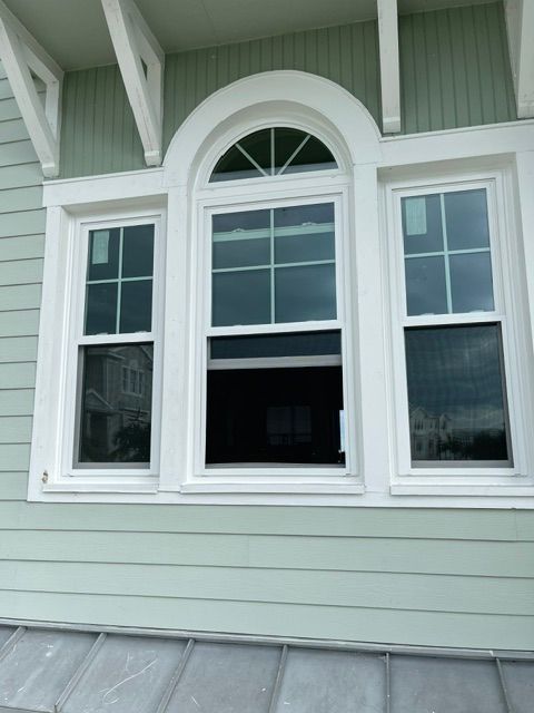 White house exterior with three windows, including a central arched window above an open lower sash.