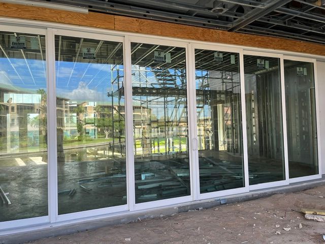 Large glass storefront windows in a building under construction, with exposed framing and reflections inside.