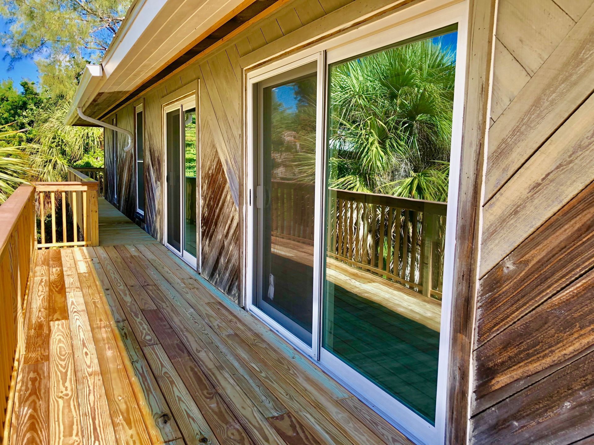 Wooden deck outside a house with sliding glass doors and railing, surrounded by trees.