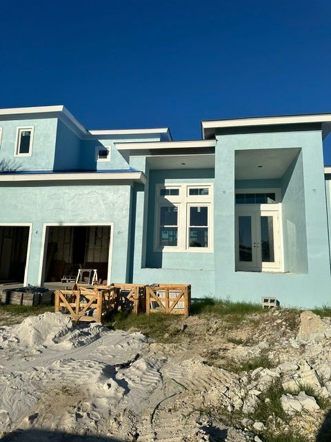 Modern pale blue house under construction with unfinished front yard and debris under a clear blue sky