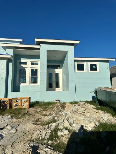 Light blue modern house exterior with a front porch, rocky yard, and clear blue sky