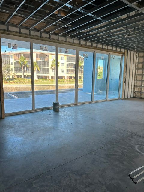 Empty unfinished room with large floor-to-ceiling windows overlooking water and nearby buildings