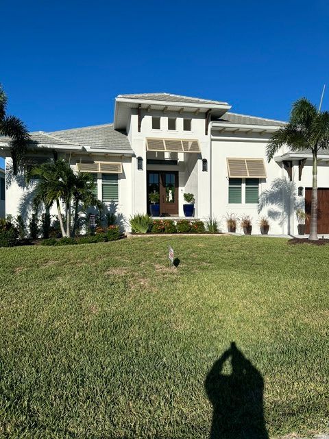 White two-story house with palm trees and a green lawn under a clear blue sky