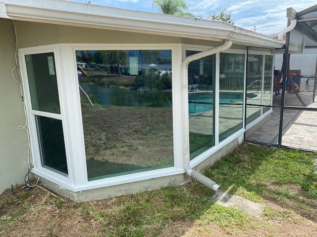 White sunroom enclosure with large windows and door beside a house, overlooking a grassy yard