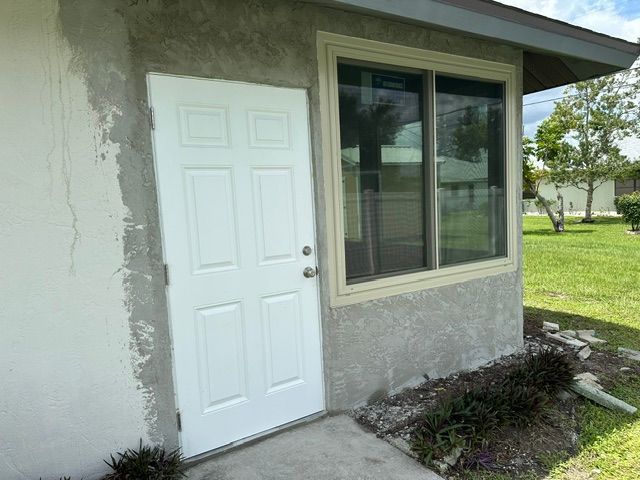 Side view of a house exterior with a white door, large window, and small landscaped yard.
