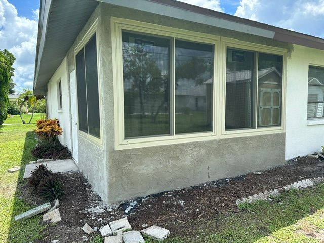 White house exterior with screened porch, gray stucco wall, and mulch beds along the foundation