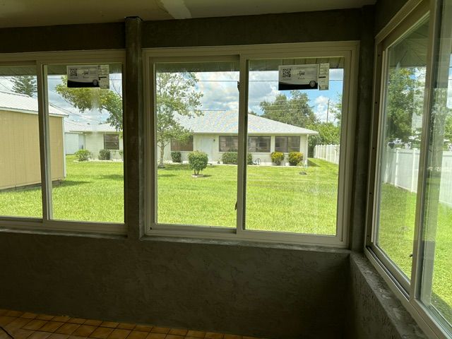 Sunroom with large windows overlooking a green yard and a single-story house outside.