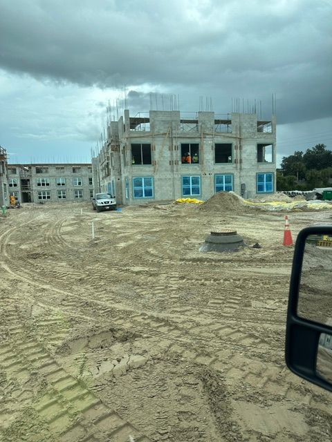 Construction site with a partially built concrete building, muddy ground, and cloudy sky.