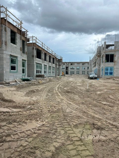 Construction site with unfinished concrete buildings, muddy ground, and cloudy sky.
