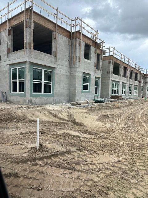 Concrete building under construction with windows, scaffolding, and muddy ground in front