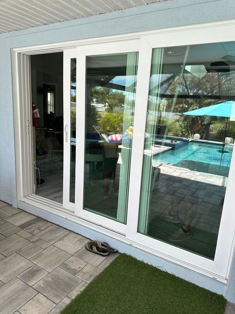 White sliding glass doors beside a patio, reflecting a backyard pool and umbrella.